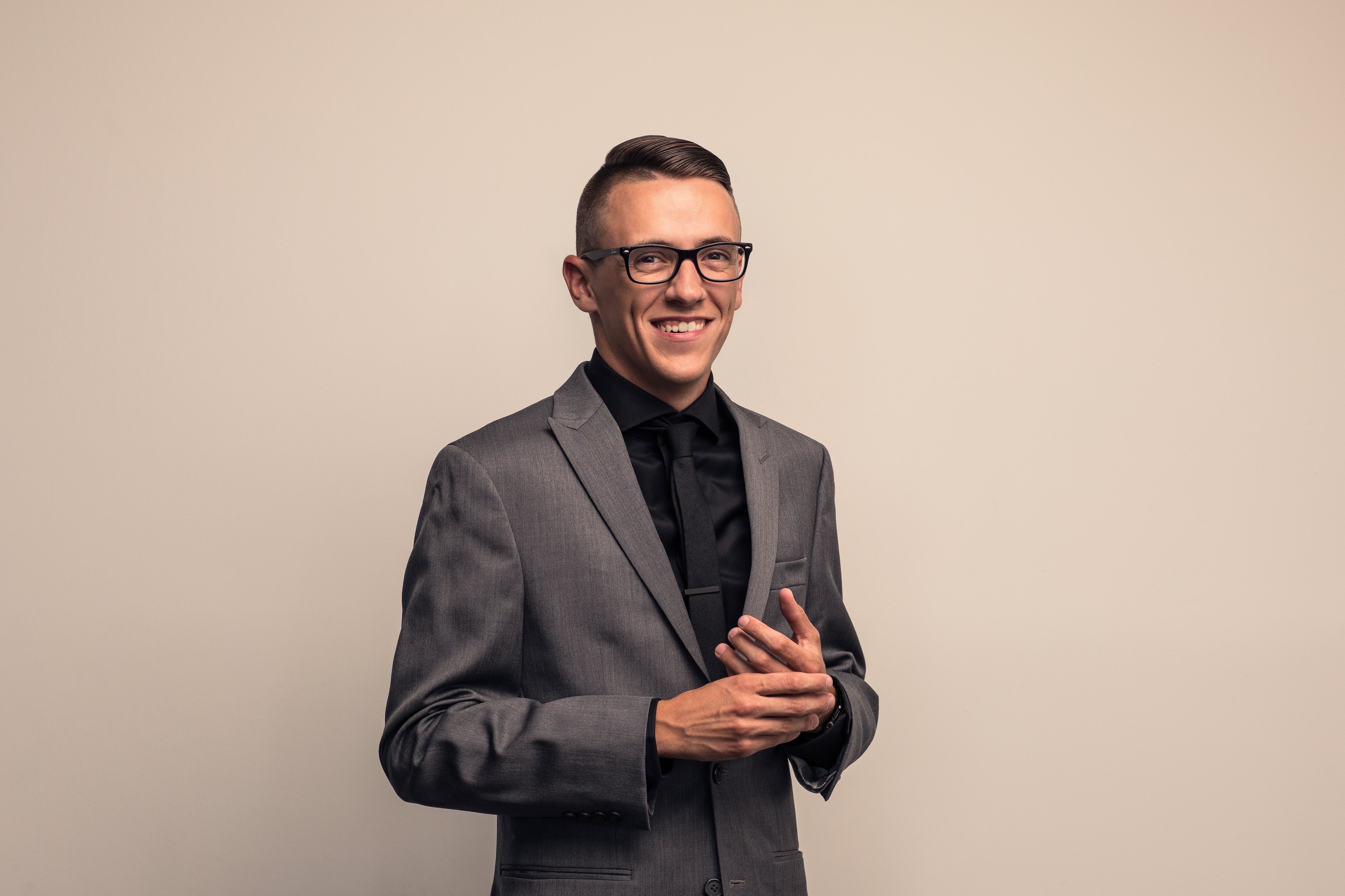Professional headshot of a man in a gray suit and glasses smiling against a neutral background.