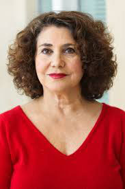 Middle-aged white woman with dark brown curly hair wearing a red dress and grinning at the caera