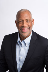 African-American man smiling wearing light blue shirt and navy jacket