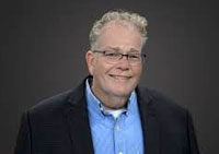 middle-aged man with glasses wearing light blue dress shirt and navy jacket smiling