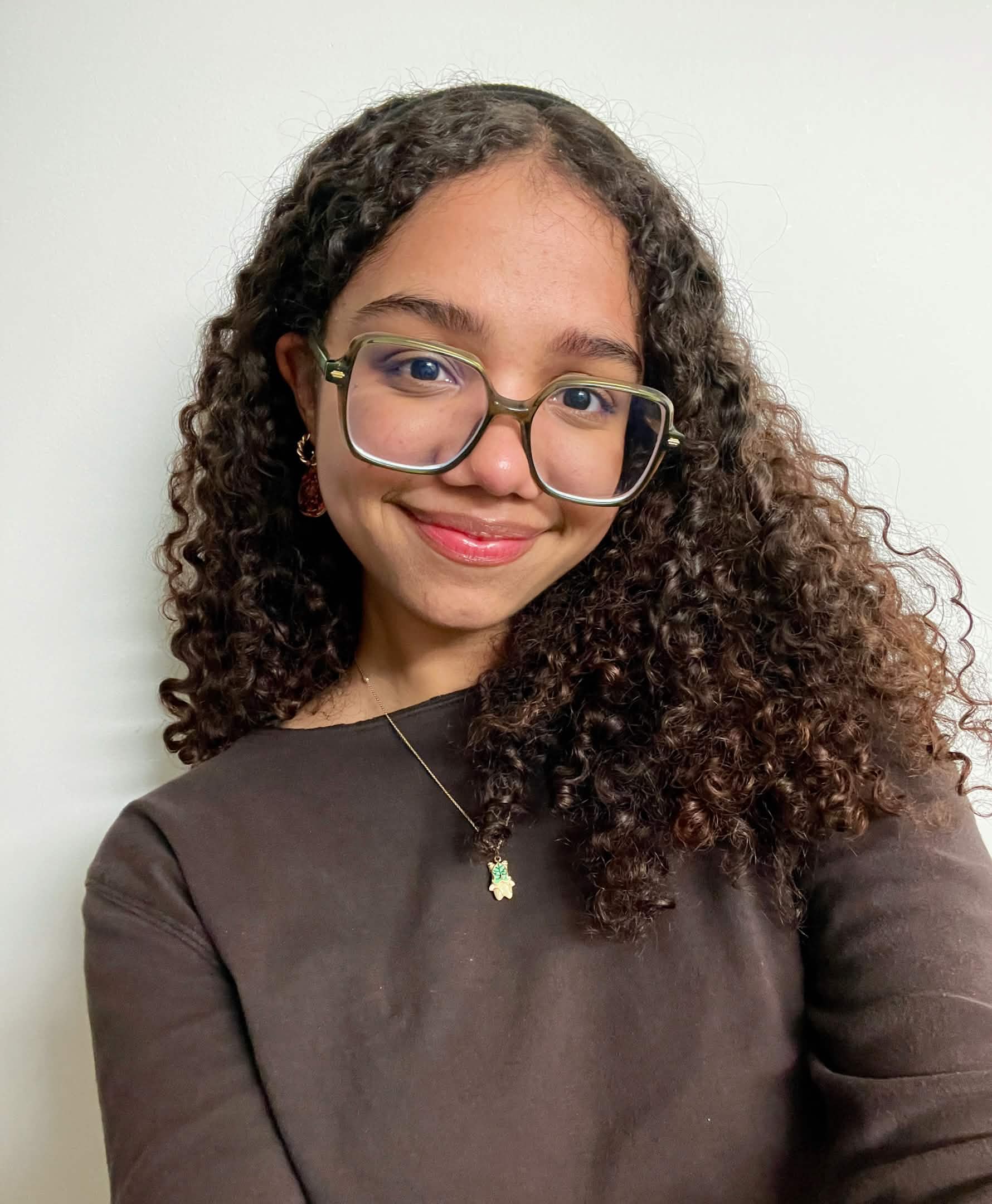 Young woman with long brown curly hair wearing glasses and smiling