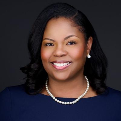 Professional headshot of Tracy Carter, president and CEO of Trailhead Community Health Foundation, smiling against a dark background. She wears a navy blue dress, pearl necklace and pearl earrings.