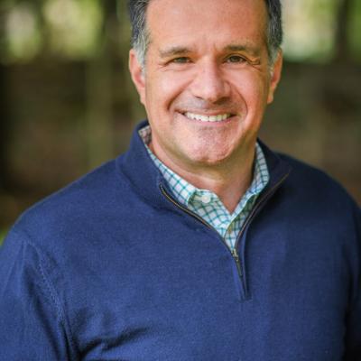 White man in his 50s wearing a blue quarter-zip sweater over a dress shirt.